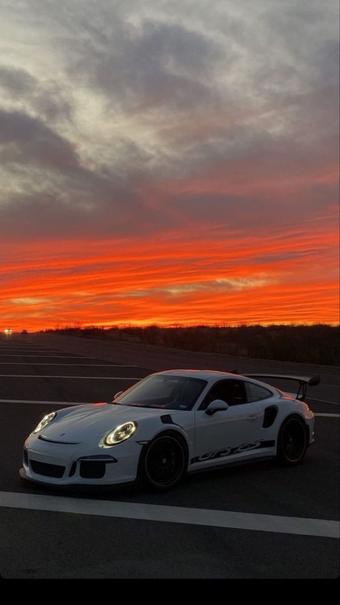 a white sports car parked in an empty parking lot with the sun setting behind it