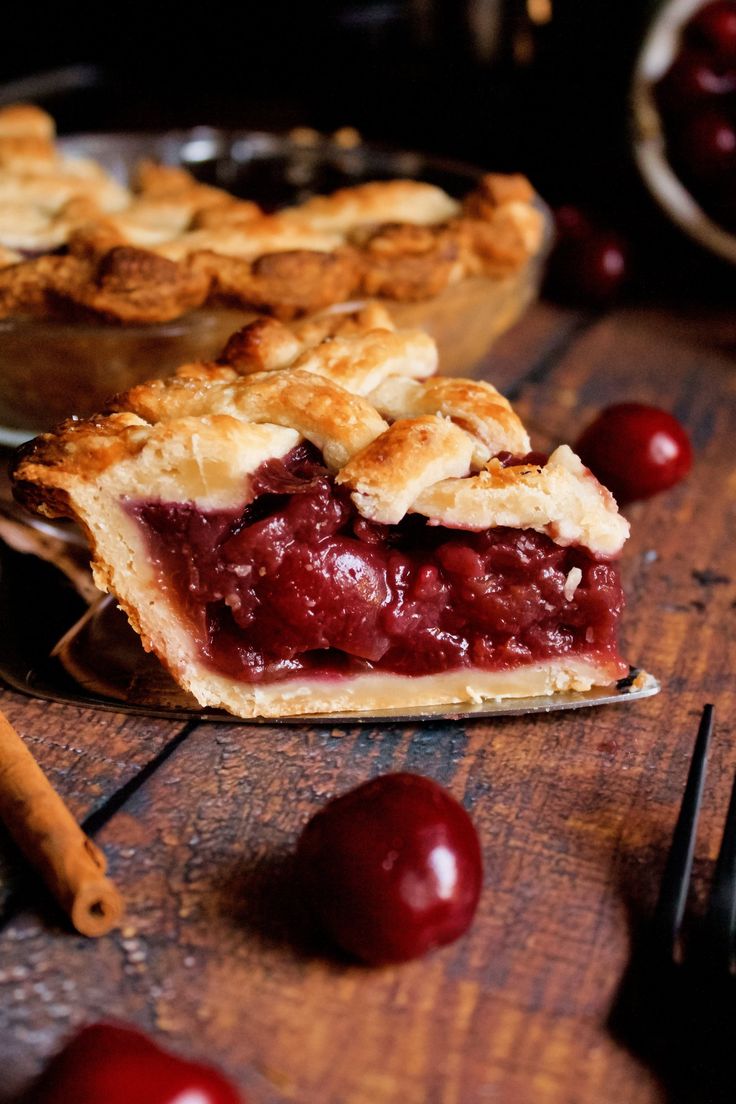 a piece of pie sitting on top of a wooden table next to a bowl of cherries