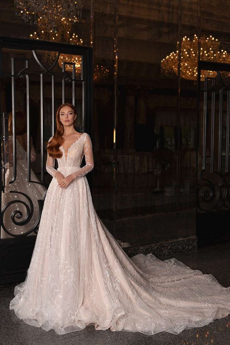 a woman standing in front of a doorway wearing a wedding dress with long sleeves and a train