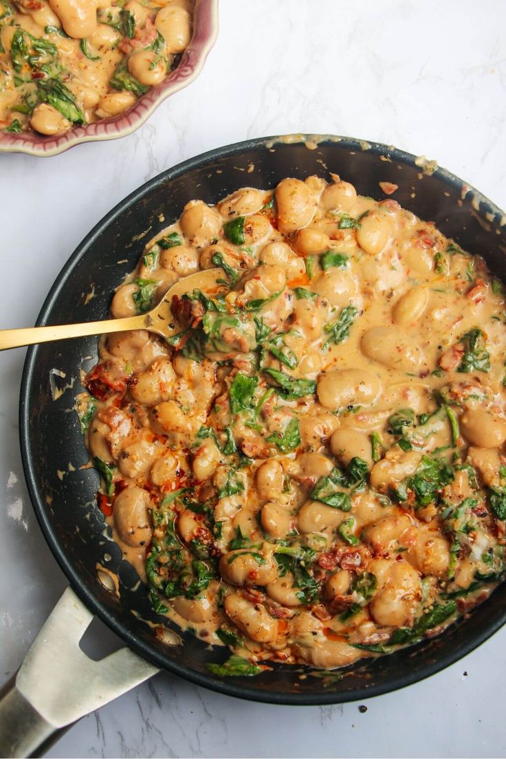 a skillet filled with pasta and spinach covered in sauce on top of a white counter