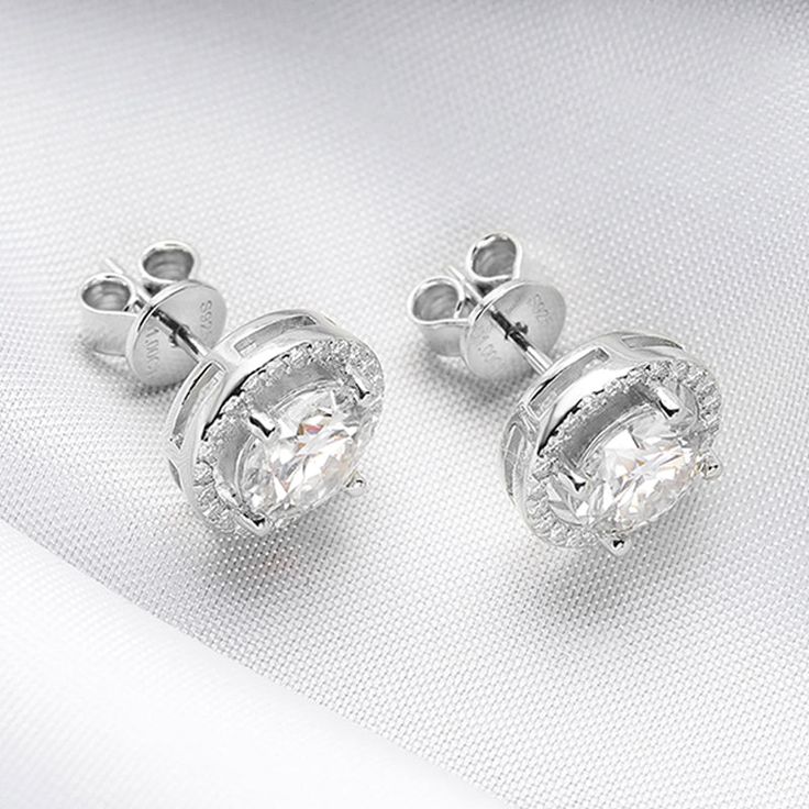 Experience the timeless elegance of a Classic 2.0 Carat Round Cut Moissanite Stud Earrings from Evani Naomi Jewelry. These high-quality earrings are simply stunning in their design and craftsmanship. Their brilliant shine is much like that of a mined diamond but comes at a significantly more affordable price. Each stud is finely handcrafted to last a lifetime, offering you a timeless piece to enjoy for years to come. They are made from a blend of 92.5% pure silver + 7.5% hypoallergenic metals an Timeless Cubic Zirconia Bridal Earrings For Anniversary, Classic Moissanite Earrings With Halo Setting, Elegant Formal Cluster Earrings With Lab Grown Diamonds, Timeless Diamond White Cubic Zirconia Bridal Earrings, Silver Moissanite Cluster Earrings, Timeless Bridal Earrings In Diamond White Cubic Zirconia, Classic Moissanite Earrings With Halo Design, Silver Moissanite Earrings With Halo Design, Elegant Moissanite Cluster Earrings Round Cut