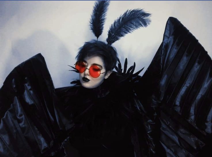 a woman in black with red glasses and feathers on her head is posing for the camera