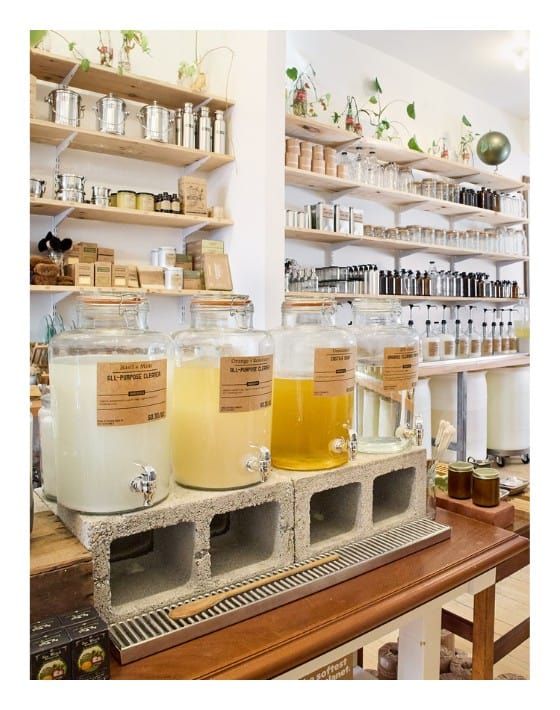 several jars filled with liquid sitting on top of a wooden shelf next to shelves full of bottles