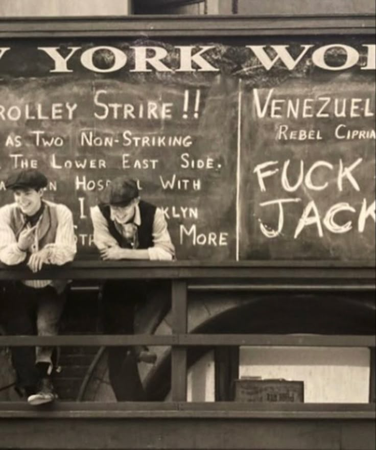 two young men sitting on a bench in front of a blackboard with chalk writing