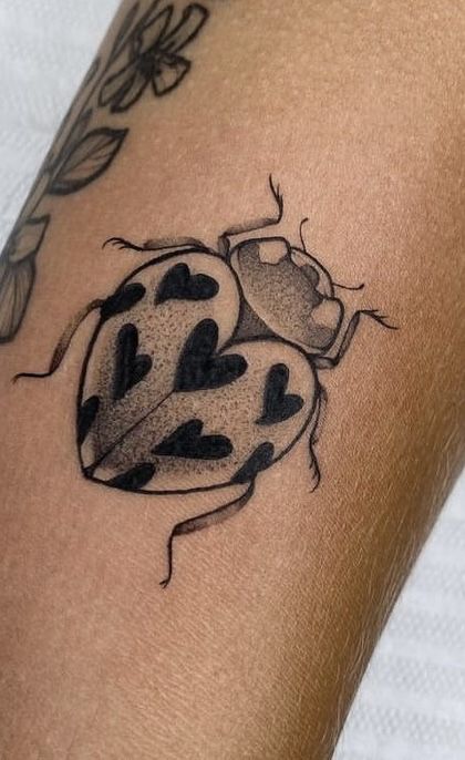 a ladybug tattoo on the arm with black dots and leaves around it's edges