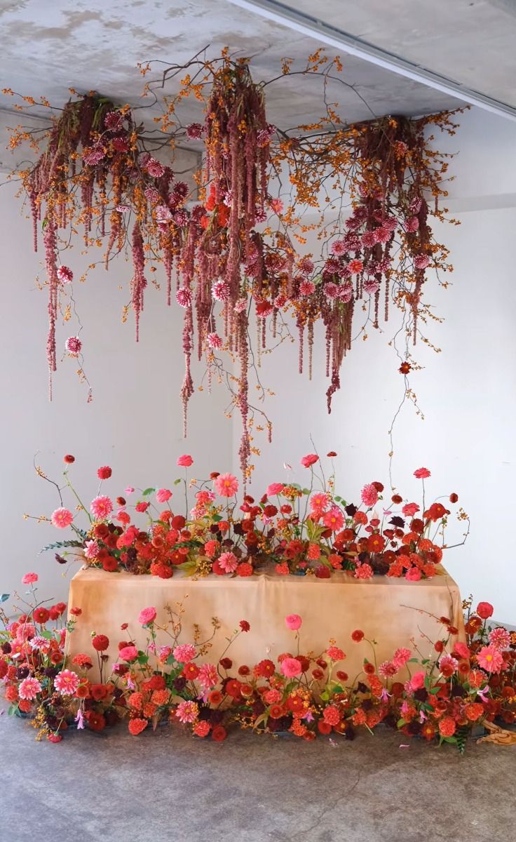 an arrangement of flowers and vines hanging from the ceiling in front of a wooden bench