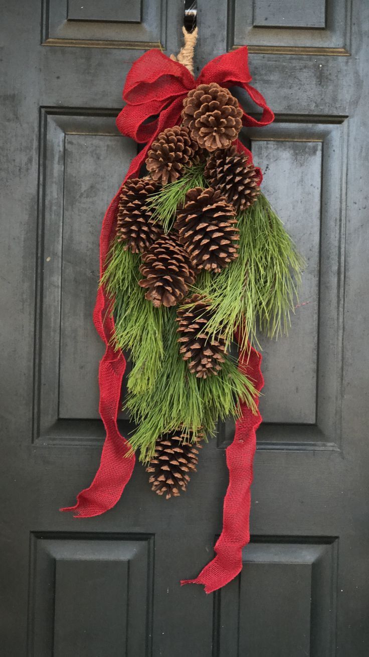 a wreath with pine cones and red ribbon hanging on a door