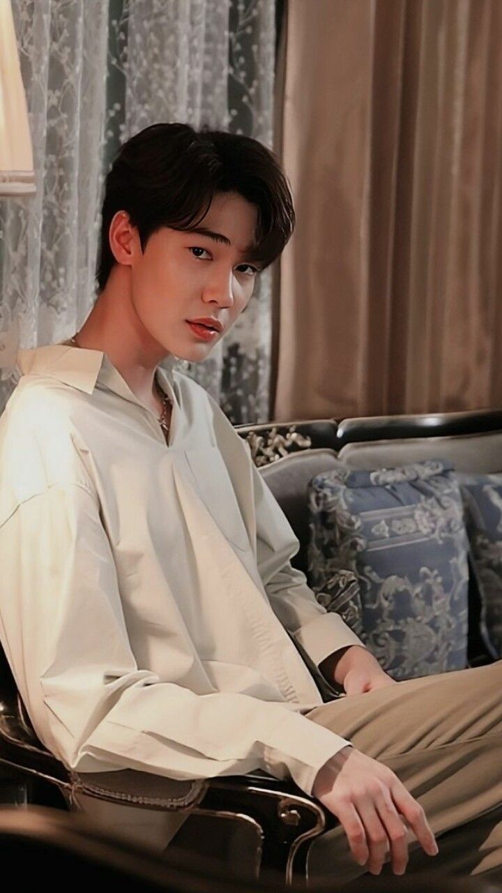 a young man sitting on top of a couch next to a lamp in a living room