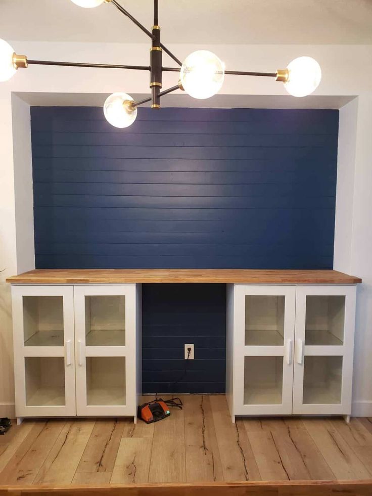 an empty room with blue walls and wooden flooring in the center is a large white cabinet