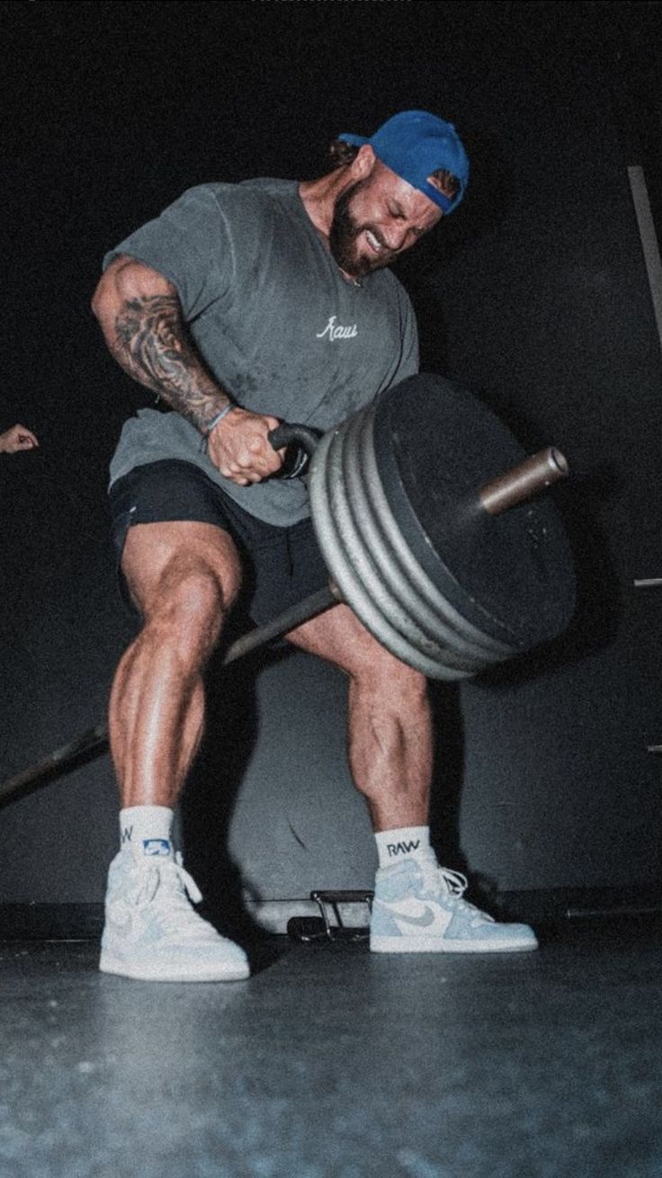 a man with a barbell squatting while holding a large metal object in his hands