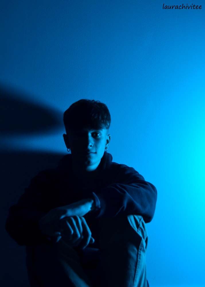 a young man sitting in the dark with his arms crossed and looking at the camera