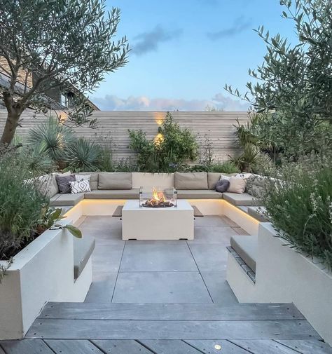 an outdoor fire pit surrounded by trees and plants on a patio with concrete seating area