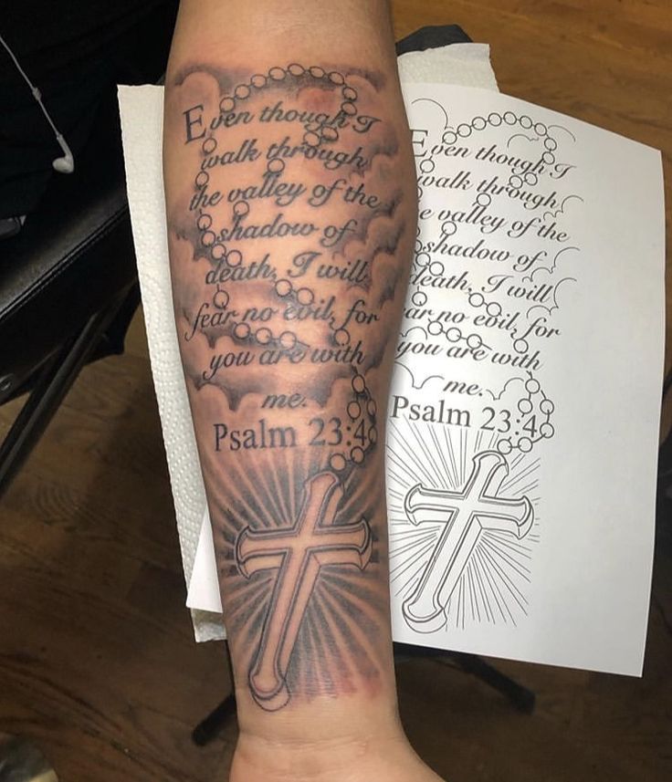 a person with a cross tattoo on their arm and the bible behind them is written in black ink