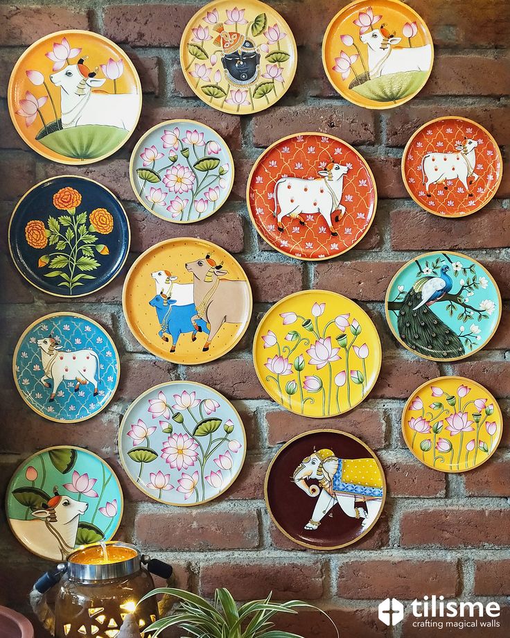 many colorful plates are hanging on the wall next to a potted plant in front of a brick wall