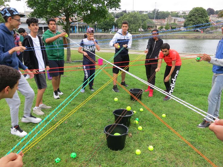 a group of young men playing with plastic balls in the grass near a body of water