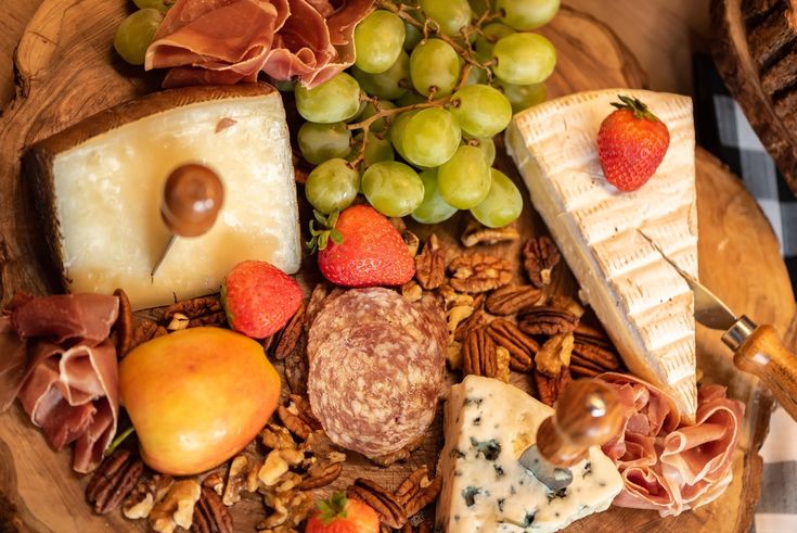 an assortment of cheeses and meats on a wooden platter with grapes, strawberries