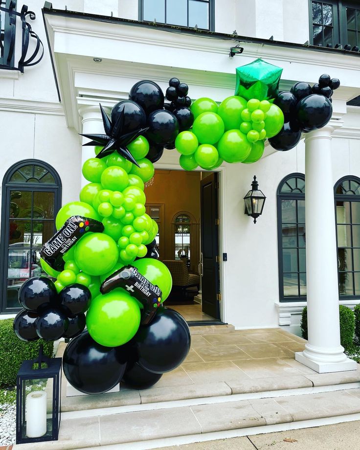 a large balloon arch with black and green balloons on it in front of a white building