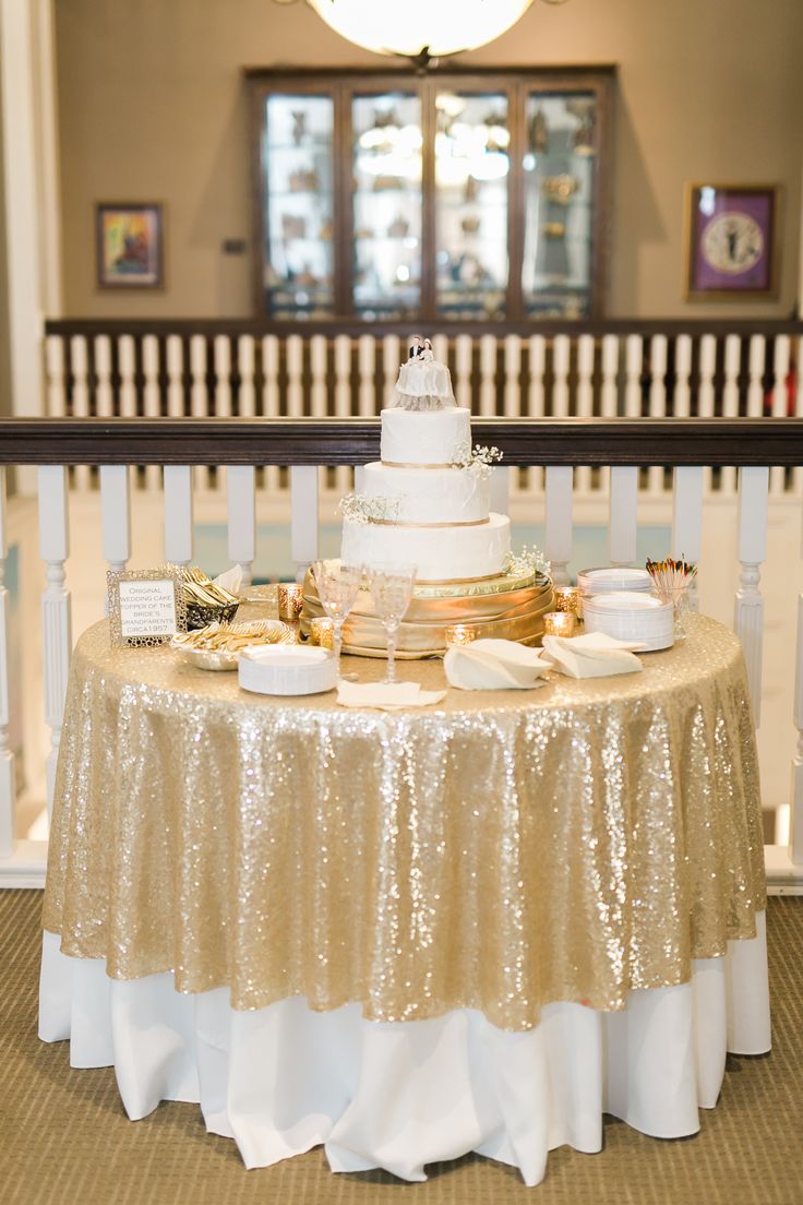 a table topped with a white and gold cake next to a stair case in a building