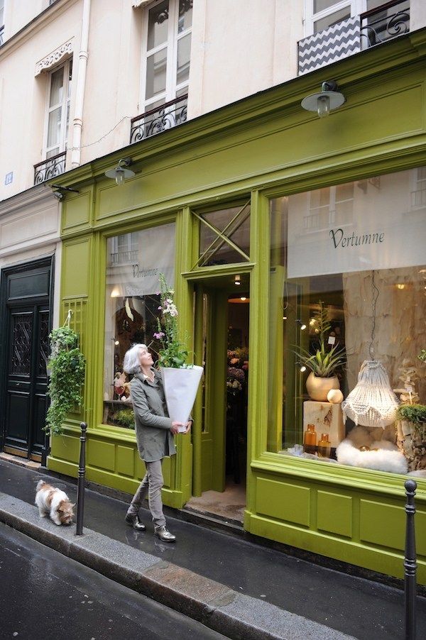 a woman walking down the street with her dog in front of a green storefront