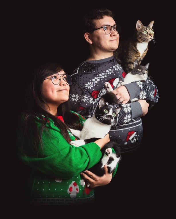 a man and woman holding two cats in their arms, both wearing ugly sweaters