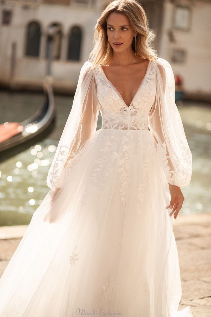 a woman in a white wedding dress standing next to a gondola and water