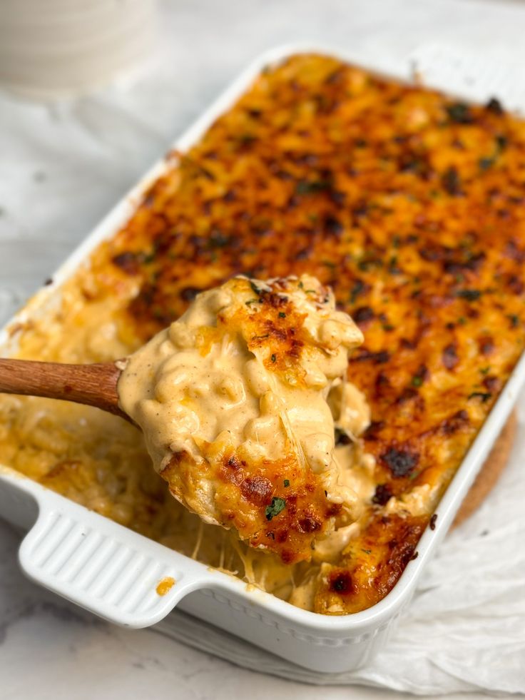 a casserole dish filled with macaroni and cheese being held by a wooden spoon