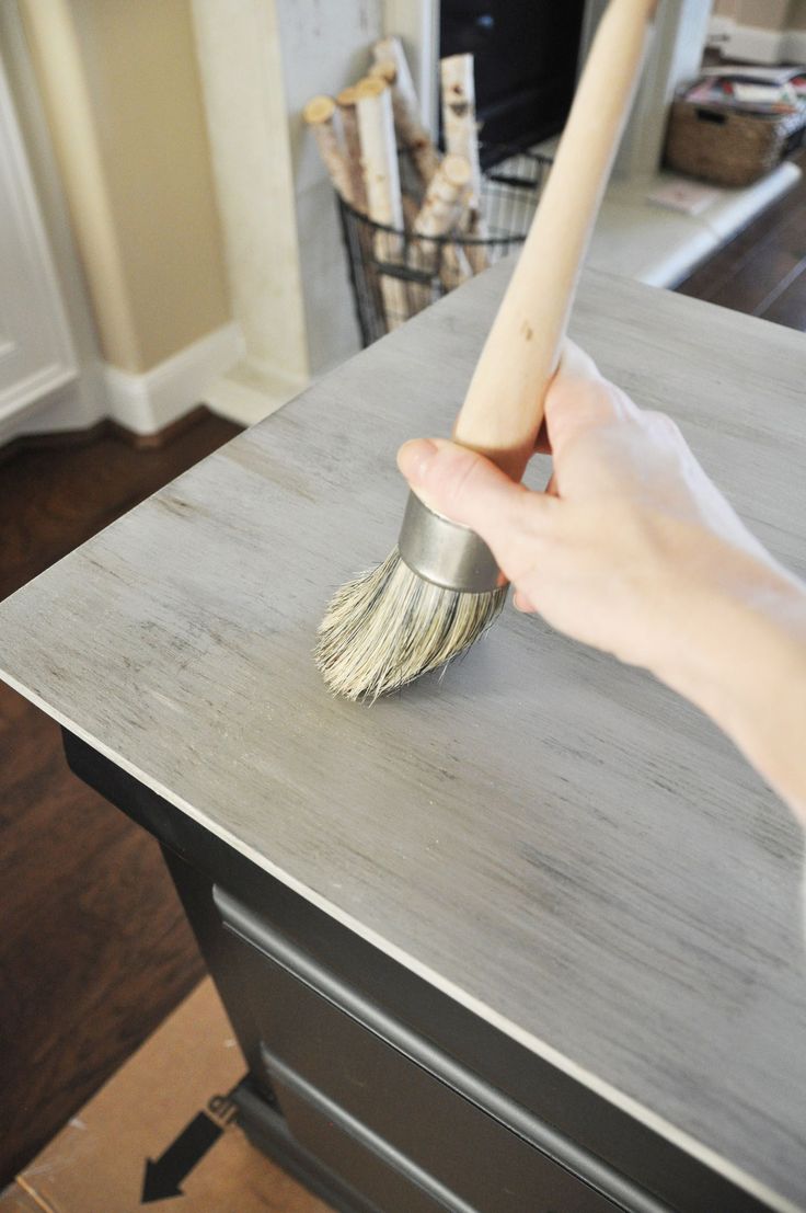 a hand holding a brush on top of a wooden table in front of a fireplace