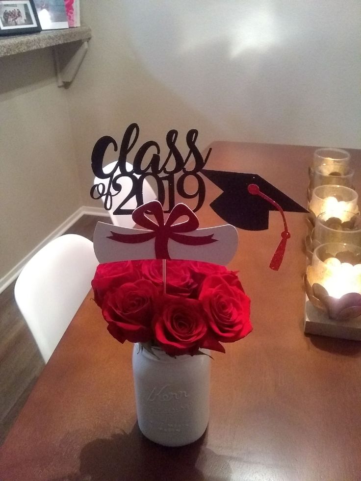 a vase filled with roses on top of a wooden table next to candles and graduation decorations