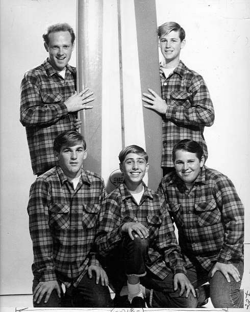 four men in plaid shirts are posing for a black and white photo with a surfboard behind them