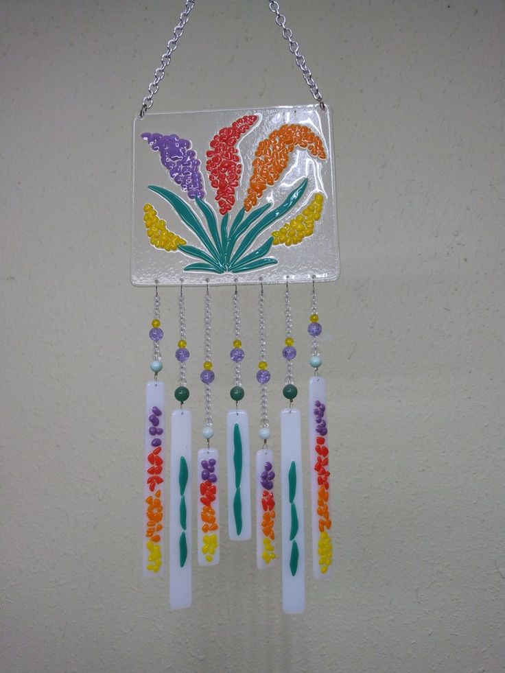 a multicolored glass wind chime hanging from a chain on a white wall