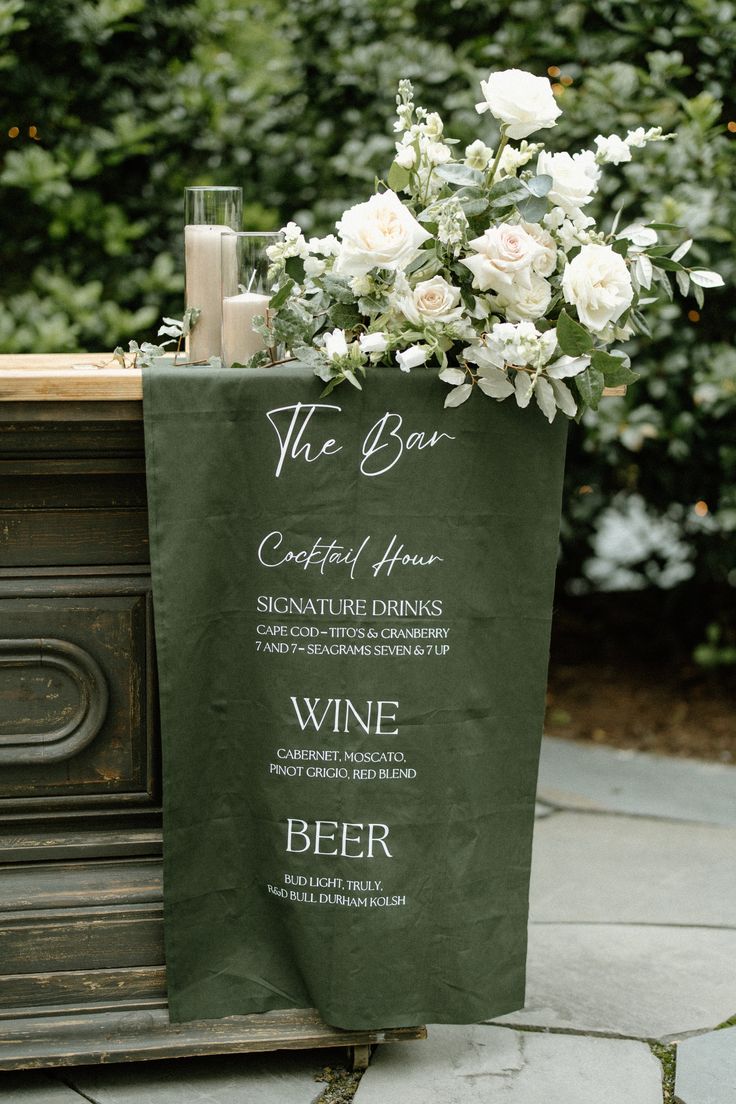 a sign with flowers on it sitting in front of a table that has wine glasses and candles