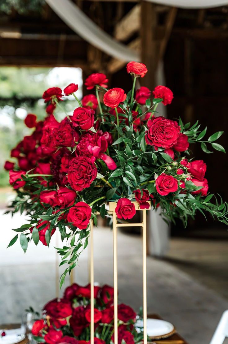 red roses are arranged in gold vases with greenery on the table for an elegant centerpiece