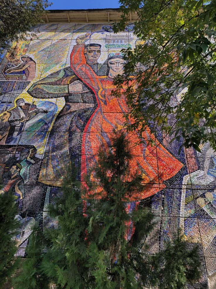 a large mural on the side of a building with many people and trees around it