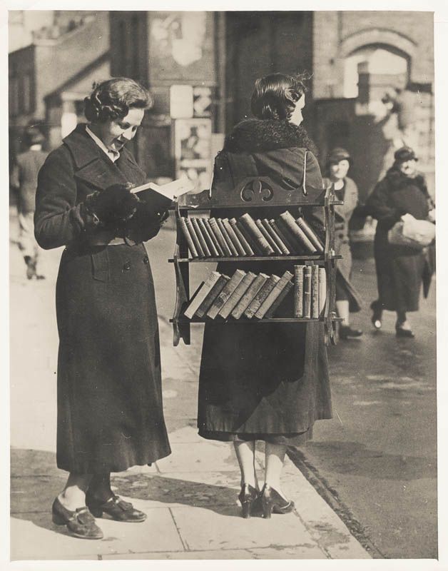 an old photo of two women looking at books on a street side stand, with the caption in russian