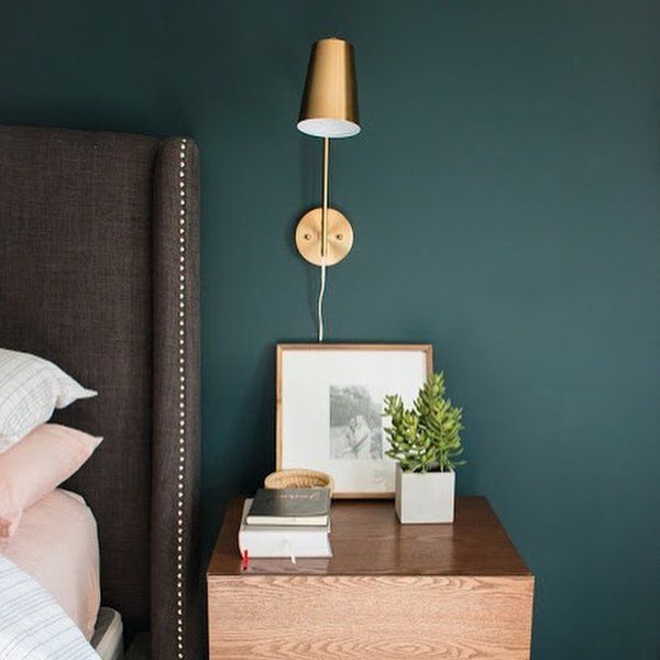 a bedroom with green walls and a nightstand next to the bed has a plant on it