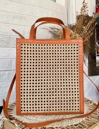 a brown woven bag sitting on top of a stack of books next to a brick wall