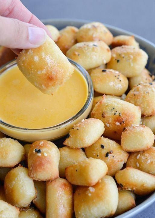 a person dipping something into a bowl filled with tater tots and cheese sauce