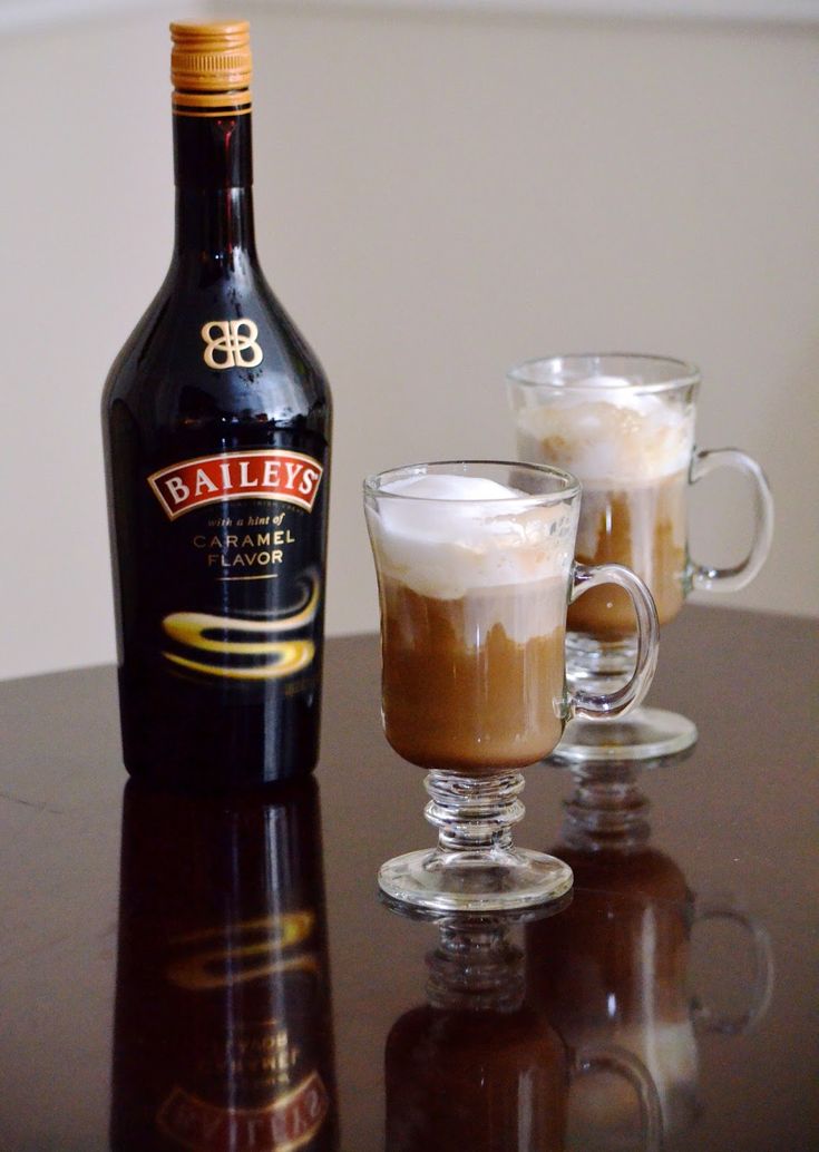 two glasses filled with liquid sitting on top of a table next to a bottle of bailey's