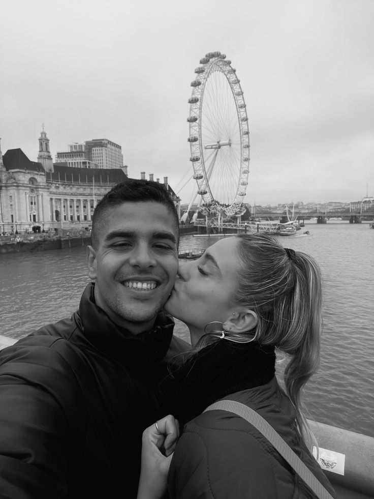 a man and woman kissing in front of a ferris wheel on the river thames, london