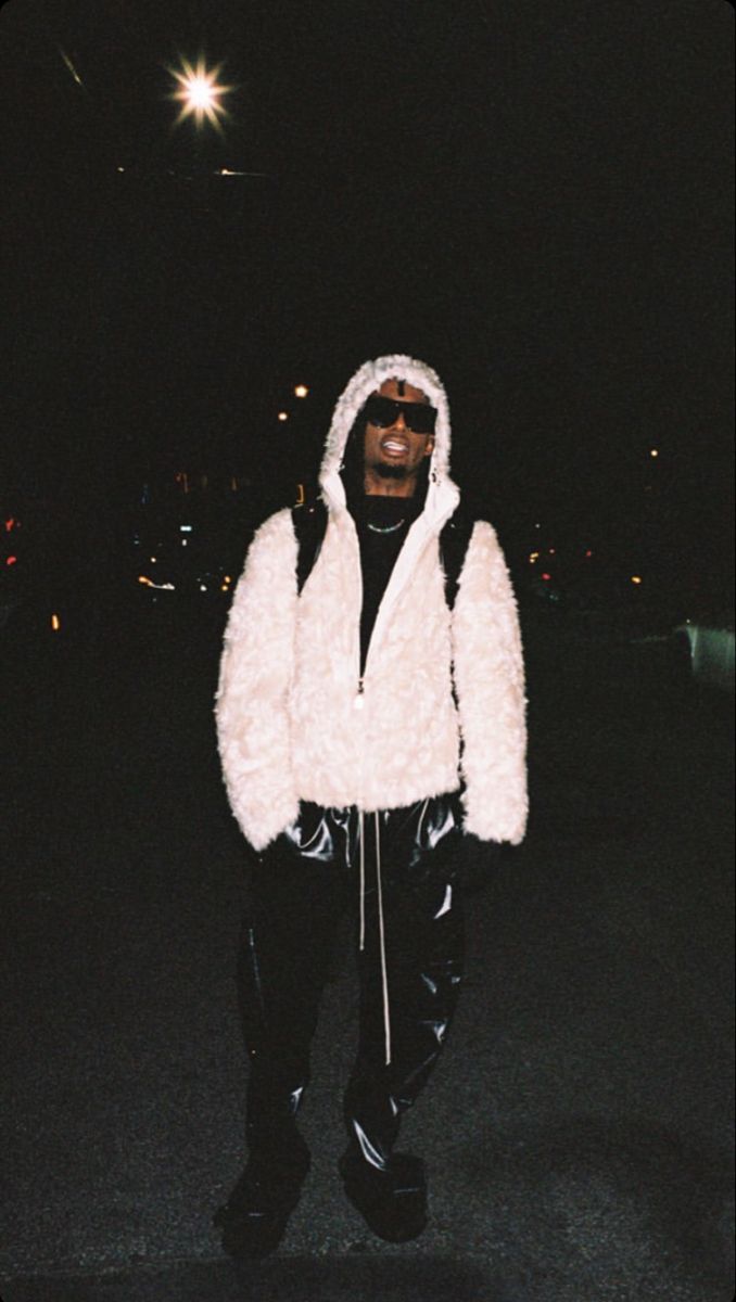 a man in a white fur coat and black pants is walking down the street at night