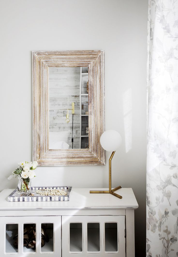 a white table with a mirror and vase on it