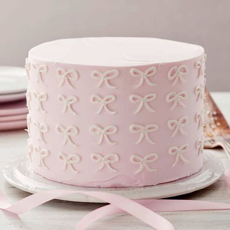 a pink cake with white bows on it sitting on a plate next to a fork