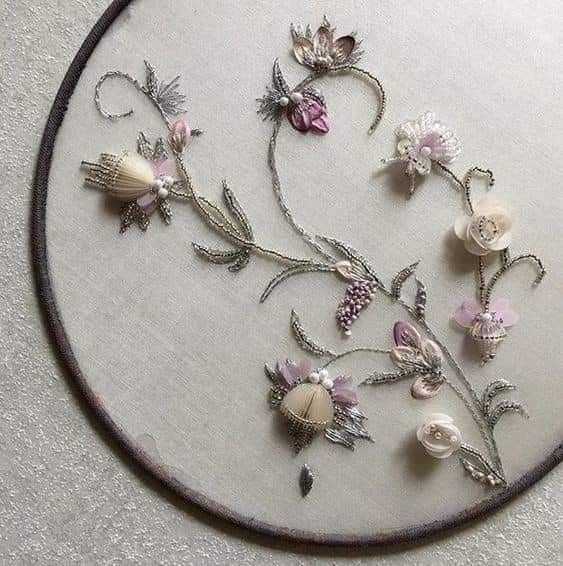 an embroidered piece with flowers and pearls on it's side in a circular frame