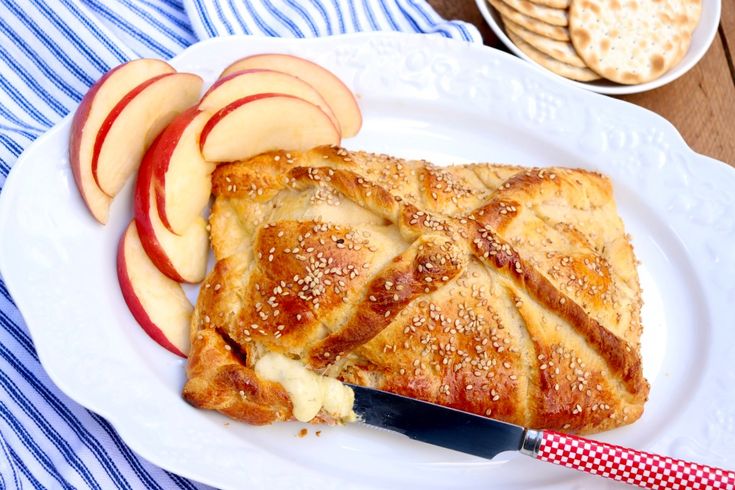 an apple pie on a white plate next to some crackers and fruit slices with a knife