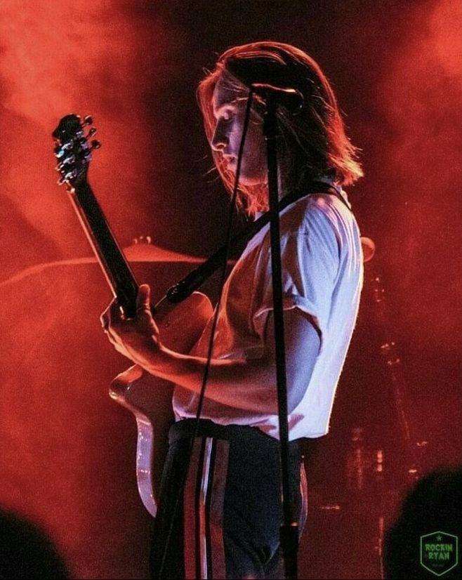 a man with long hair holding a guitar in front of a microphone and on stage