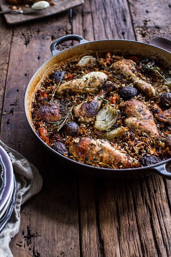 a pan filled with chicken and vegetables on top of a wooden table next to other dishes