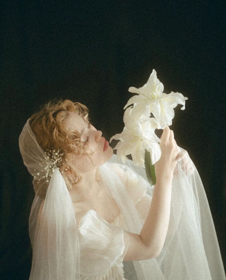 a woman in a wedding dress smelling a flower