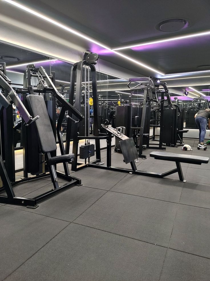 an empty gym with equipment and people in the background at night or early evening time