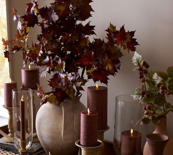 a table topped with vases filled with leaves and candles