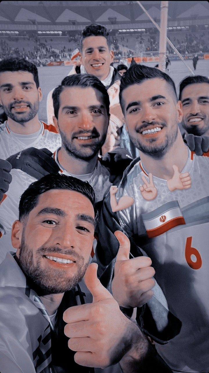 a group of men standing next to each other in front of a soccer field with their thumbs up